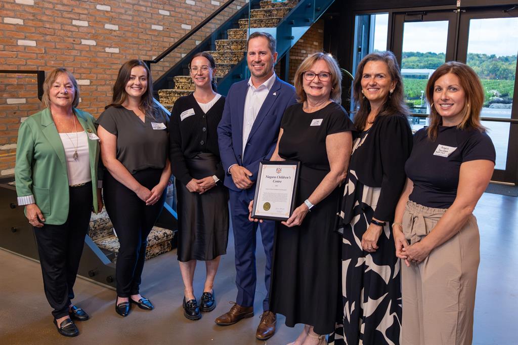Group of seven people pose with a framed letter in front of a staircase