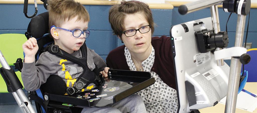 Female Niagara Children’s Centre Speech Language Pathologist uses Augmentative and Alternative Communication computer technology to provide care to a male child in a wheelchair.